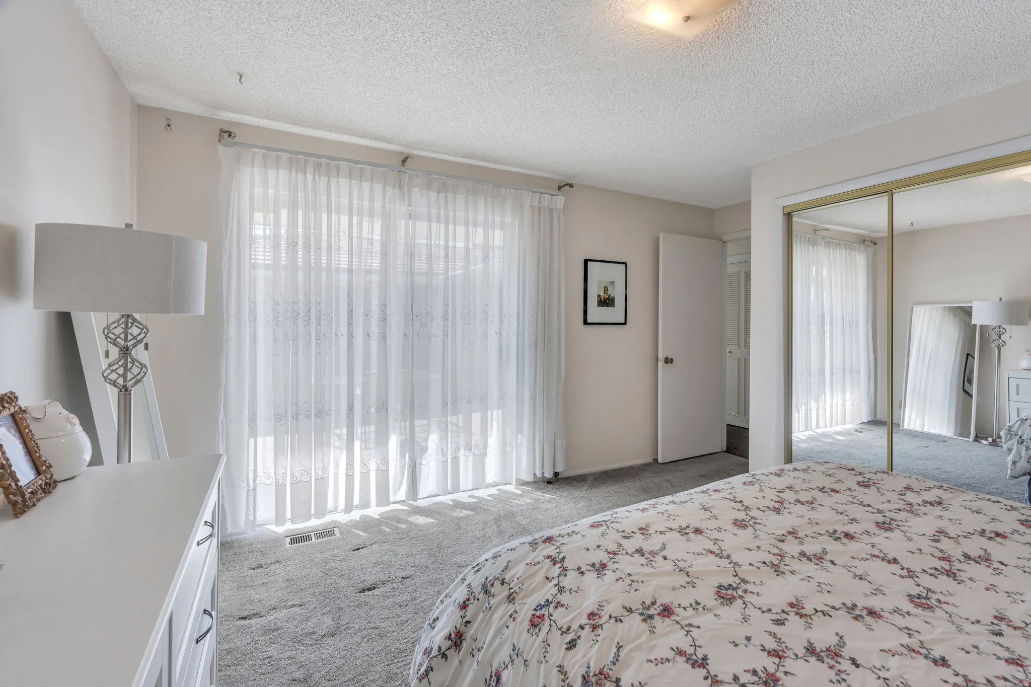 Carpeted flooring, full-height sliding glass doors, overhead ceiling light, and mirrored closet doors
