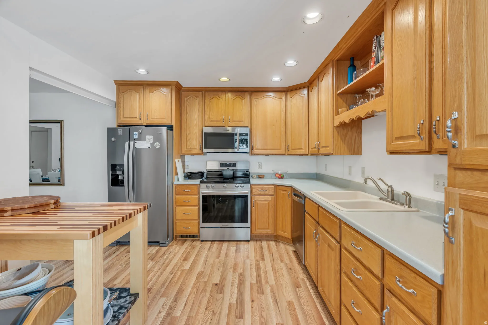 Kitchen featuring wood-finish flooring, stainless steel appliances, extensive wood cabinetry, light countertops, and a double basin sink