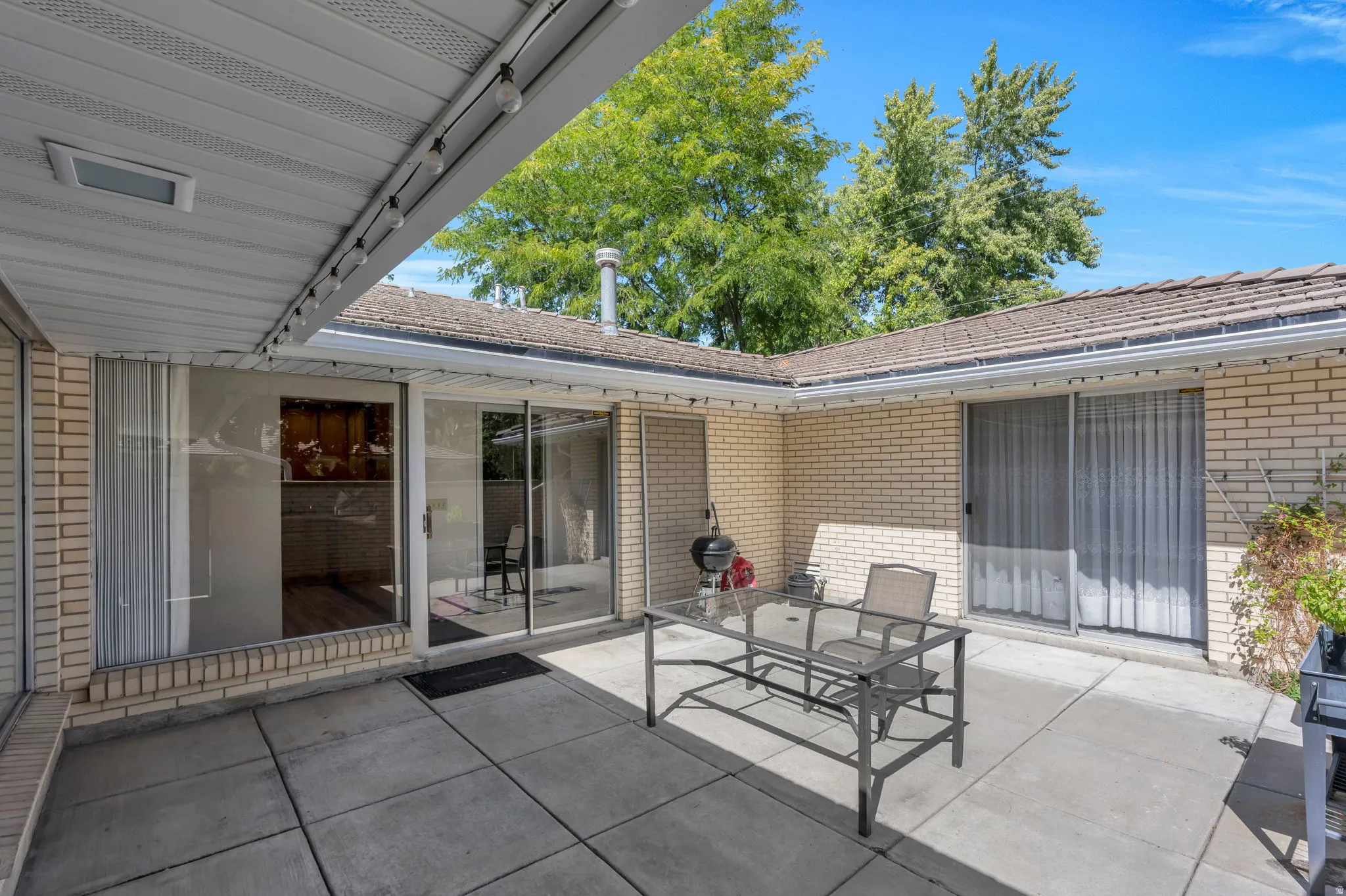 Paved patio with overhead covering, brick exterior, and multiple sliding glass doors