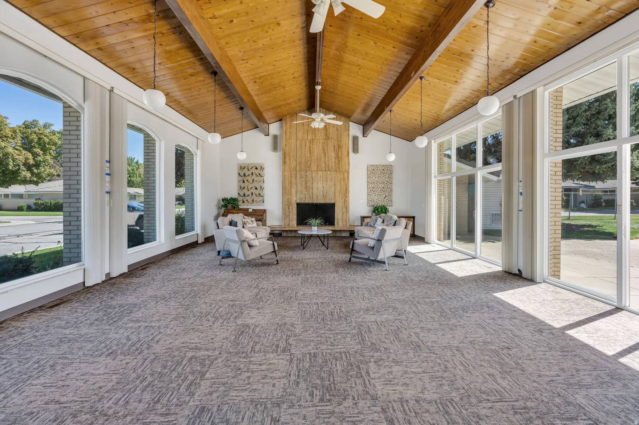 Vaulted wood-paneled ceiling with exposed beams, wood-clad fireplace, built-in ceiling fan, large arched windows, and patterned carpet flooring