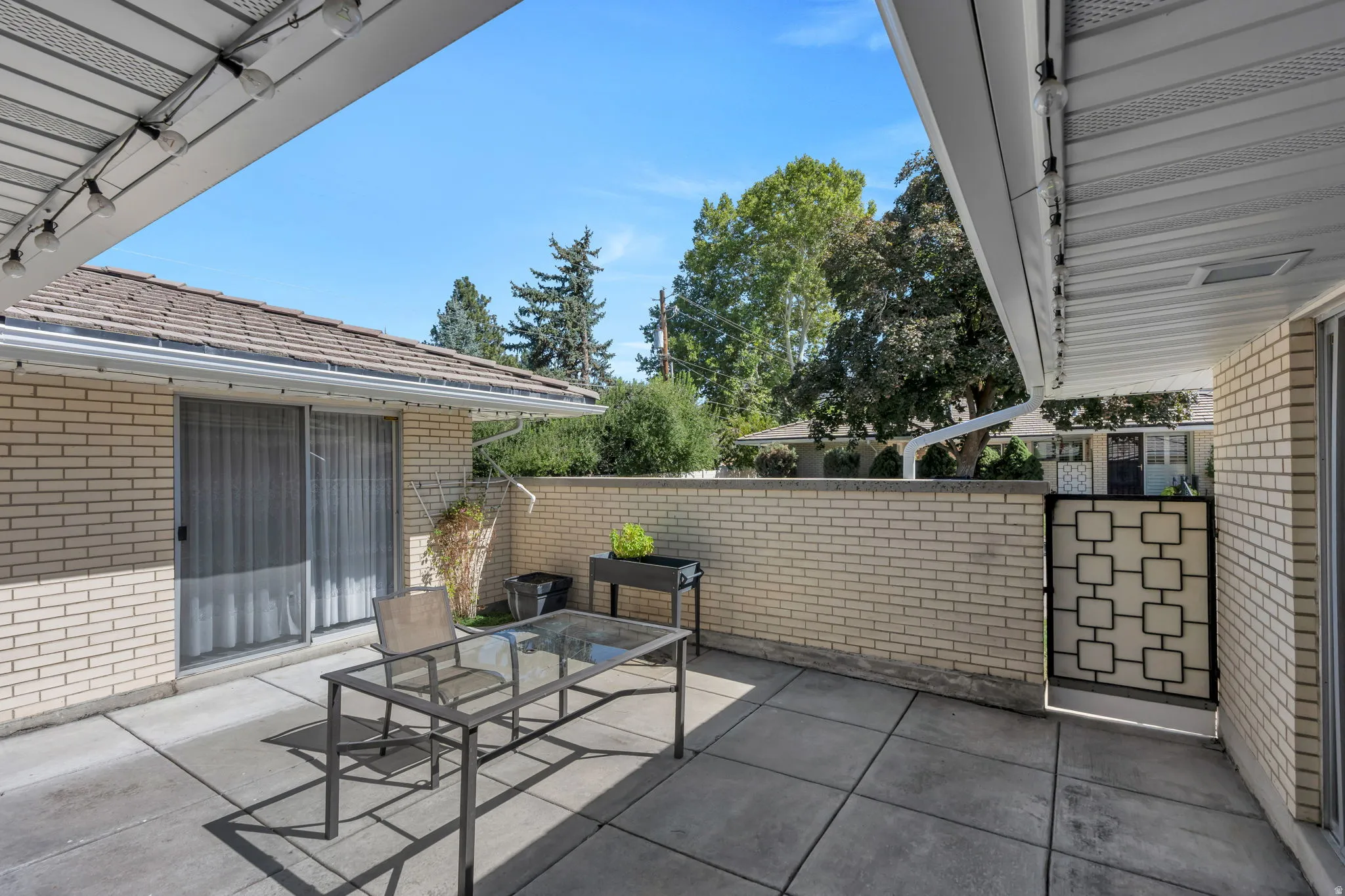 Paved patio featuring a brick privacy wall, sliding glass door access, and an overhead awning with string lighting