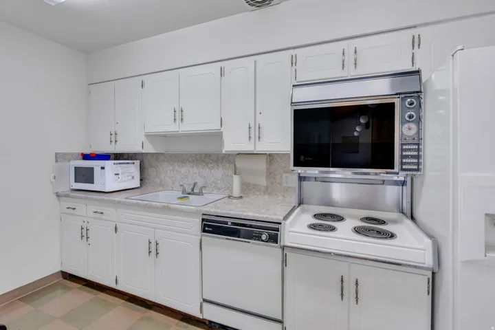 White cabinetry with silver-tone hardware, a drop-in sink, a built-in wall oven, a surface cooking range, and a dishwasher