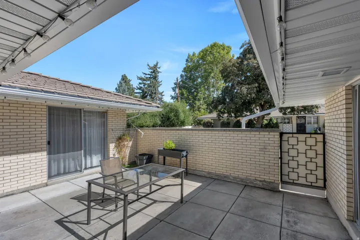 Paved patio featuring a brick privacy wall, sliding glass door access, and an overhead awning with string lighting