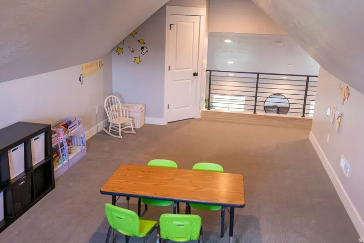 Carpeted loft space with a white paneled door, sloped ceilings, and a black metal railing