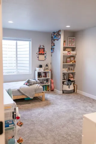 Recessed lighting, large window with horizontal blinds, built-in shelving, built-in corner shelves, and soft grey carpeting