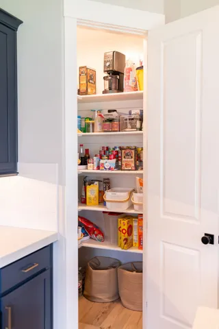 Built-in pantry featuring white shelving, light wood-finish flooring, and a white paneled door