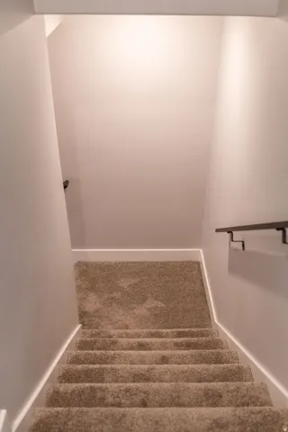 Carpeted staircase with recessed lighting and a sleek black handrail