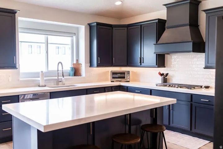 Kitchen featuring dark cabinetry, white countertops, white subway tile backsplash, a center island with seating, and a built-in gas range