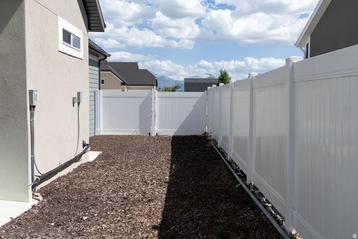 Enclosed side yard featuring a white privacy fence, gate access, and wood chip ground cover