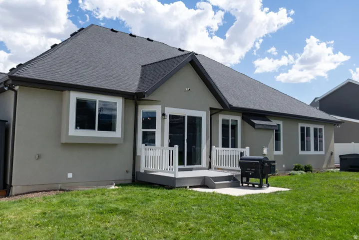 Stucco exterior with a dark shingle roof, featuring a private rear deck with white railings, a sliding glass door, and multiple bay windows