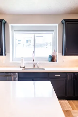 Kitchen featuring a stainless steel undermount sink with a gooseneck faucet, dark cabinetry, light countertops, and a white subway tile backsplash