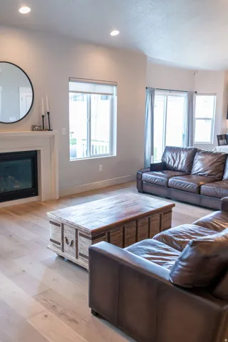 Living area featuring a fireplace with a white mantel, recessed lighting, wood-finish flooring, and multiple windows