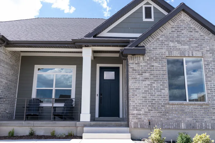 Exterior featuring gray brick and horizontal siding, a covered porch with white columns, a dark gray entry door, and a prominent gable accent