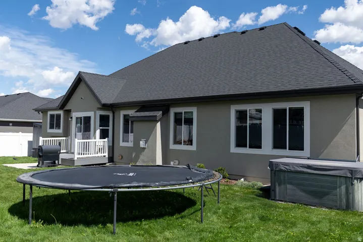 Rear exterior featuring a neutral stucco facade, white-framed windows, dark shingle roofing, and a raised white deck