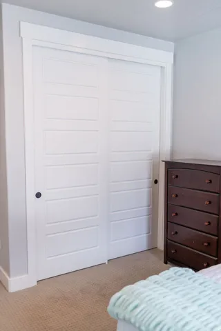 White panel bi-fold doors with black hardware, recessed ceiling lighting, and light-toned carpet flooring