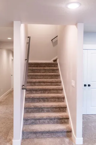 Carpeted staircase with contemporary metal handrail and recessed ceiling lighting