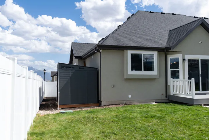 Stucco exterior with a dark shingled roof, white vinyl fencing, a private side yard with a storage shed, and a rear deck with sliding glass doors