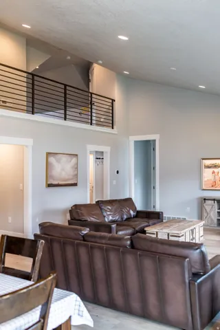Vaulted ceiling with recessed lighting, light wood-finish flooring, and a second-story interior balcony with black metal railing