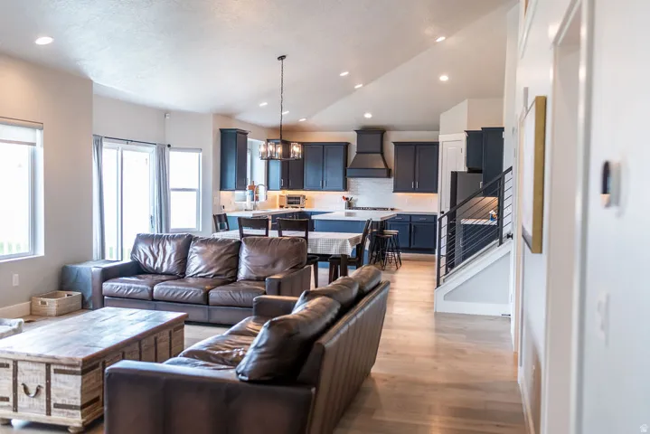 Open concept living area featuring wood-finish flooring, vaulted ceilings, recessed lighting, and a kitchen with dark cabinetry
