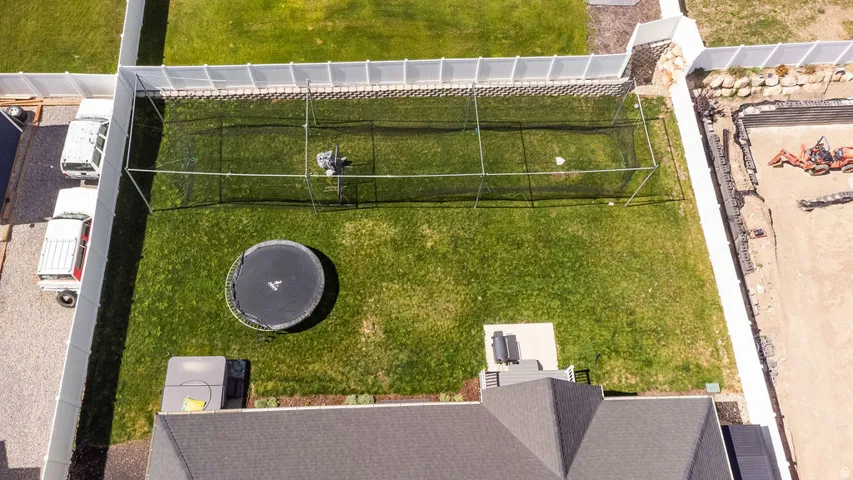 Expansive backyard featuring a manicured lawn, white privacy fencing, and a batting cage structure