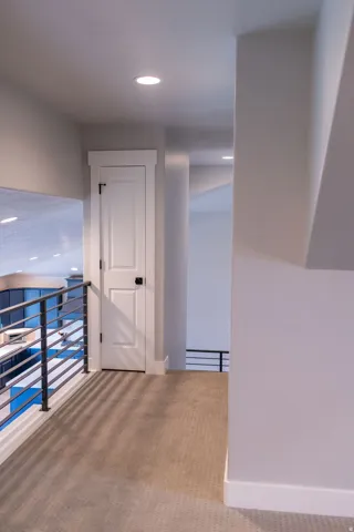 Upper-level hallway featuring recessed lighting, neutral carpeting, and a modern horizontal bar railing
