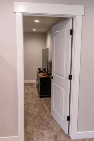 Interior paneled door with matte black hardware, recessed ceiling lighting, and wall-to-wall carpeting