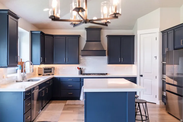 Kitchen featuring navy cabinetry, white countertops, a tiled backsplash, wood-finish flooring, and a stainless steel refrigerator