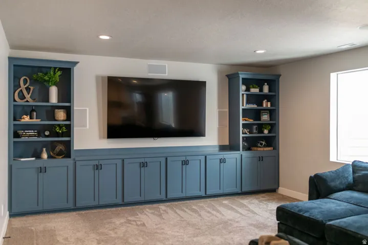 Built-in media console with integrated shelving, matte blue cabinetry, recessed lighting, and wall-mounted speakers