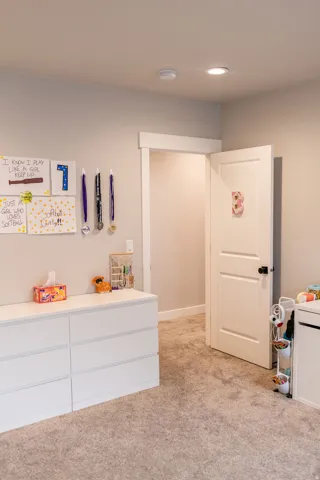 Plush carpet flooring, recessed ceiling lighting, a white painted door with matte black hardware, and crisp white trim