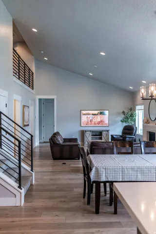 Vaulted ceiling with recessed lighting, wood-finish flooring, open-tread staircase with metal railing, upper-level hallway with metal railing, and white trim