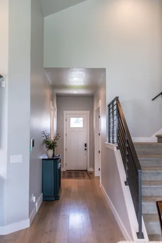Entryway featuring wood-finish flooring, a white paneled door, vaulted ceilings, and a staircase with metal railings