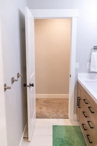White paneled door with dark hardware, a light wood-finish vanity with dark pulls, white countertop, and light tile flooring
