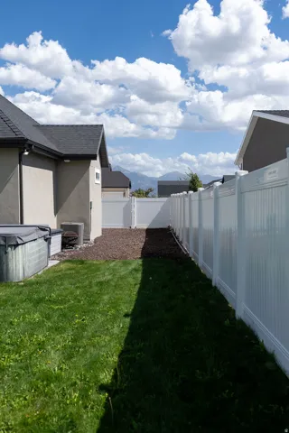 Expansive backyard featuring a manicured lawn, white vinyl fencing, and a spa