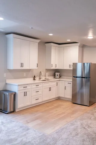 White shaker-style cabinetry with matte black hardware, stainless steel sink with gooseneck faucet, light-toned wood-finish flooring, and recessed ceiling lighting