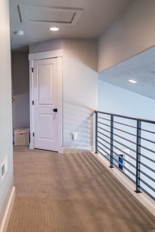 Hallway featuring neutral-toned carpeting, white interior door with dark hardware, recessed lighting, and a contemporary horizontal metal railing
