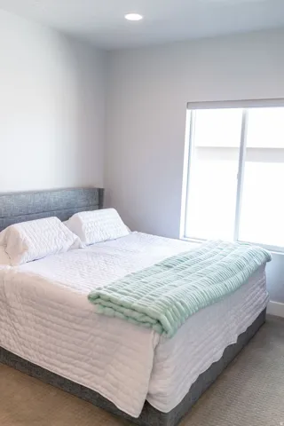 Recessed ceiling lighting, large window with roller shades, neutral carpeting, and light-toned walls