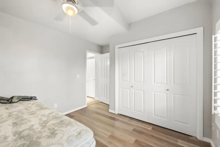 Wood-finish flooring, white bi-fold closet doors, ceiling fan, and white interior doors