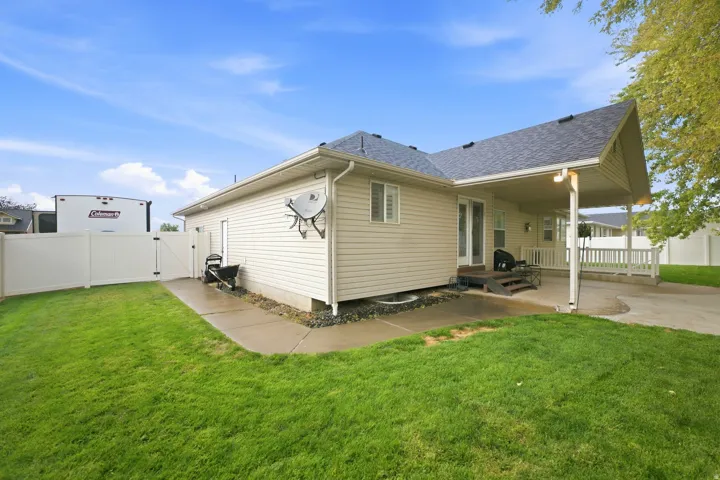 Expansive backyard featuring a manicured lawn, concrete patio, covered porch with white railing, and white vinyl fencing