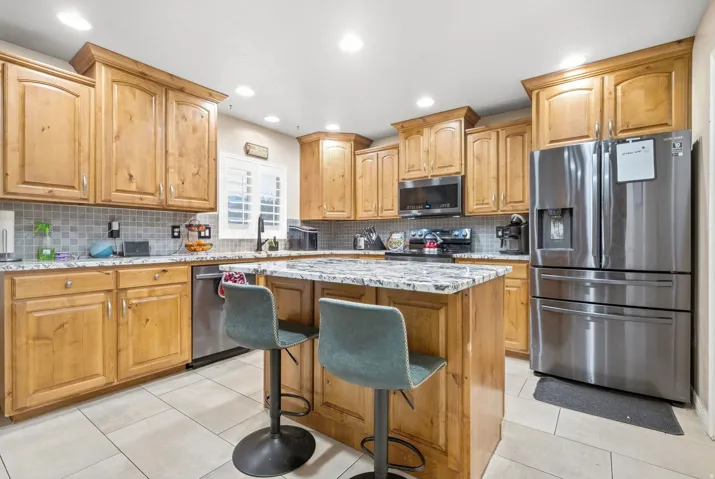 Kitchen featuring warm wood cabinetry, stainless steel appliances, a center island with countertop seating, a tile backsplash, and recessed lighting