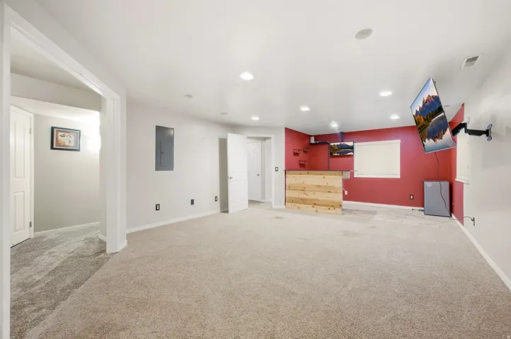 Expansive carpeted area with recessed lighting, a built-in wood-paneled bar, and a window for natural light