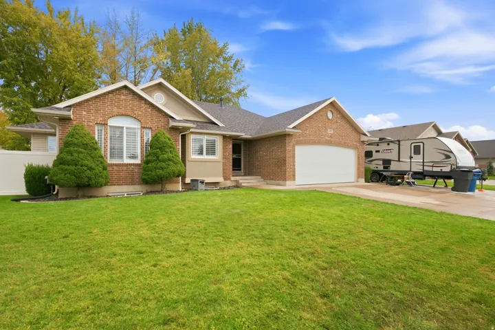 Brick exterior with white trim, two-car garage, front lawn, and mature trees