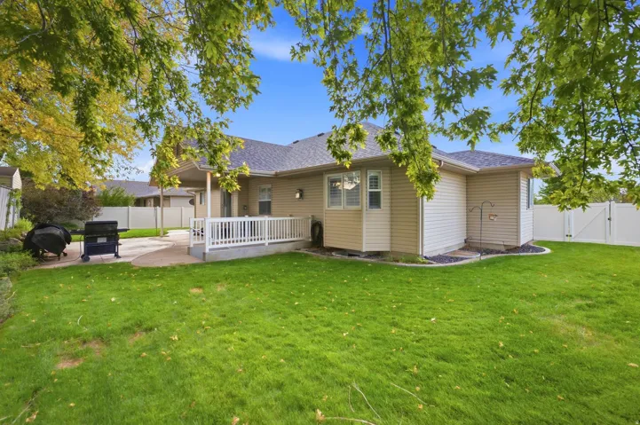 Expansive grass yard with a concrete patio, white railing, and perimeter fencing
