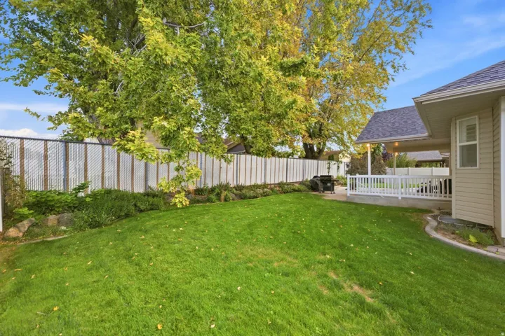 Expansive lawn featuring mature trees, a covered patio with white railings, and privacy fencing