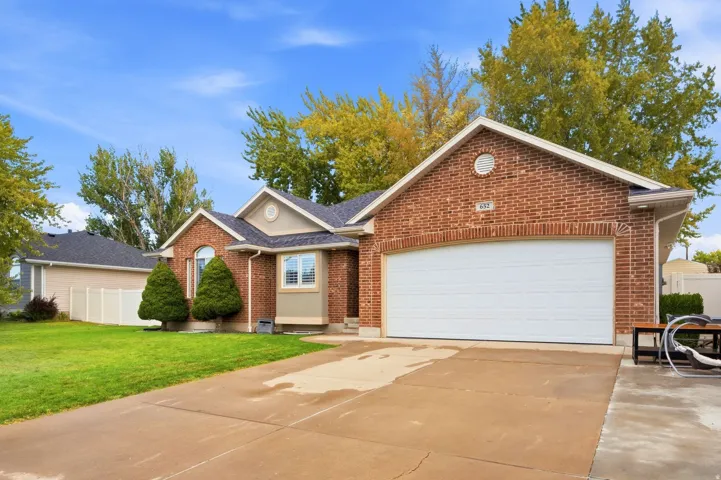 Brick exterior with gabled roofline, attached two-car garage, concrete driveway, and manicured landscaping