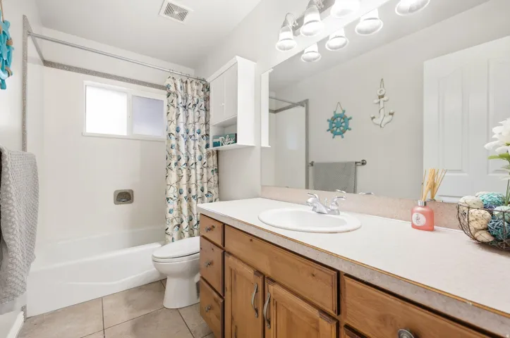 White bathtub with integrated shower, single window, and tiled flooring