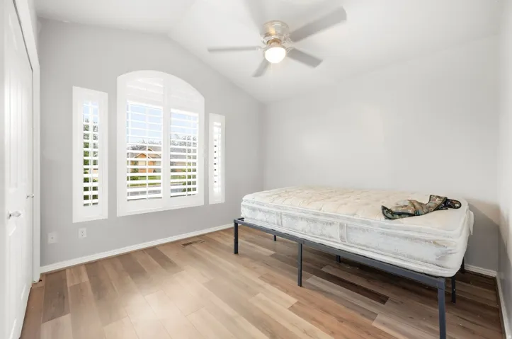 Vaulted ceiling with a ceiling fan, wood-finish flooring, plantation shutters, and a white paneled door
