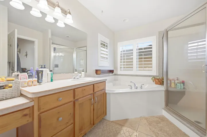 Wood-finish vanity with an integrated sink, large vanity mirror, built-in corner soaking tub, and a glass-enclosed shower