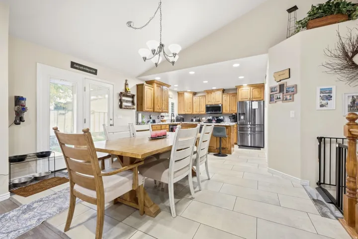 Open-concept living space featuring vaulted ceilings, a kitchen with wood cabinetry and stainless steel appliances, and tile flooring