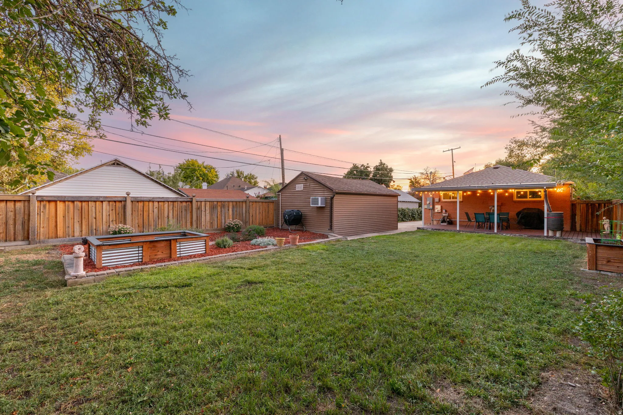 Expansive backyard featuring a covered patio, a detached shed, a full privacy fence, and a raised garden bed