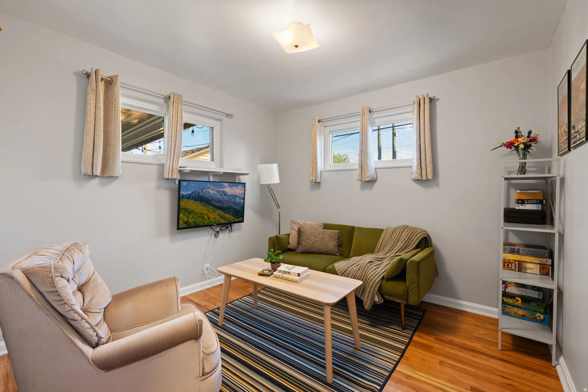 Hardwood flooring, light gray wall paint, multiple windows, ceiling light fixture, and white trim
